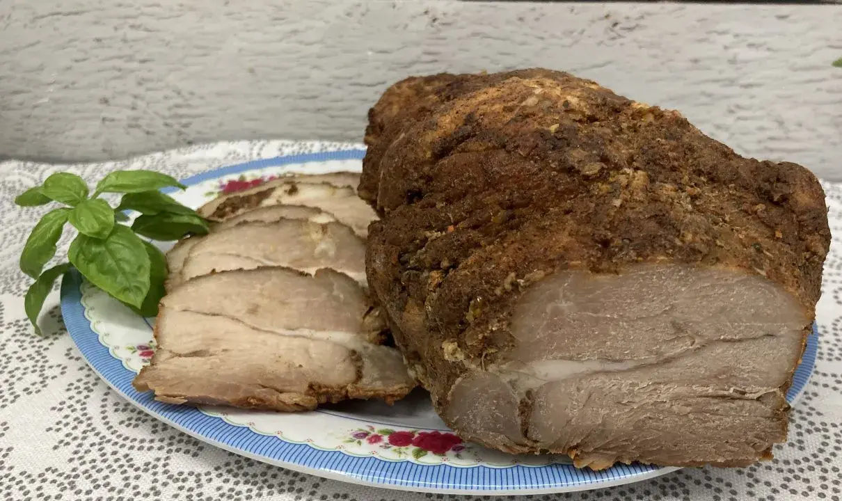 Soczysta łopatka pieczona w rękawie, pokrojona w plastry, z gałązką bazylii na talerzu.