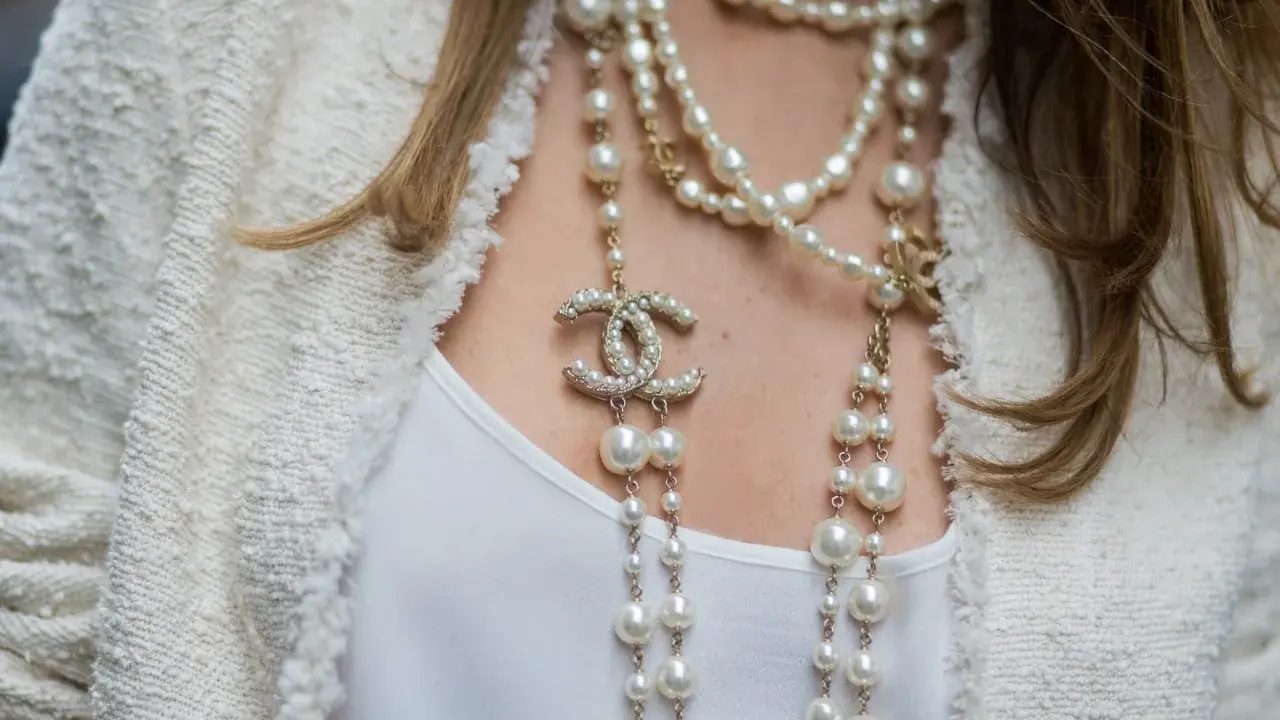 Eleganckie stylizacje z perłami, w tym wielowarstwowy naszyjnik Chanel z logo marki i perłami, dodają blasku białej bluzce i żakietowi.