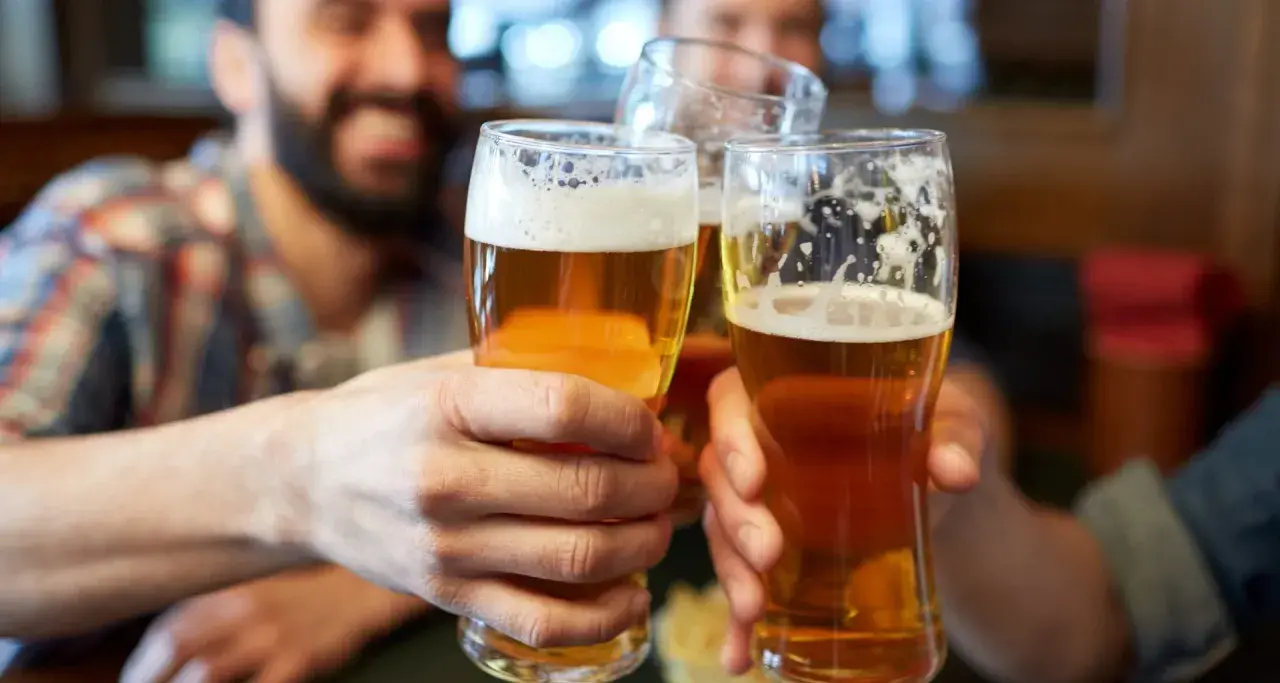 Trzech przyjaciół wznosi toast. Każdy trzyma w dłoni szklankę złocistego piwa z pianką.