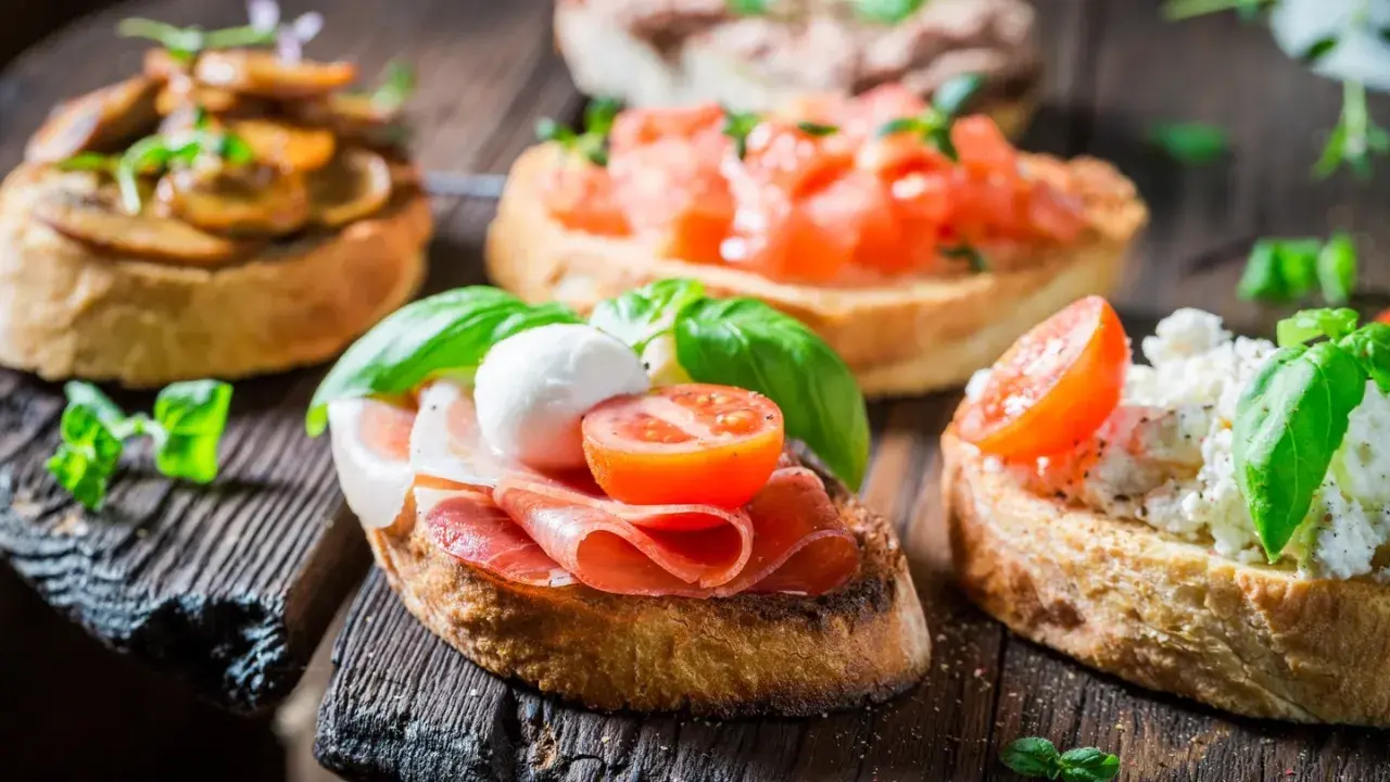 Verschiedene herzhafte Snacks auf geröstetem Brot: Bruschetta mit Tomaten, Pilzen, Schinken und Mozzarella.