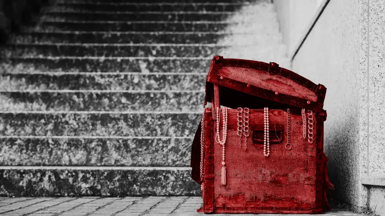 Czerwona skrzynia z biżuterią, stojąca na schodach. To pamiątka, spadek po rodzicach, pełen wspomnień.