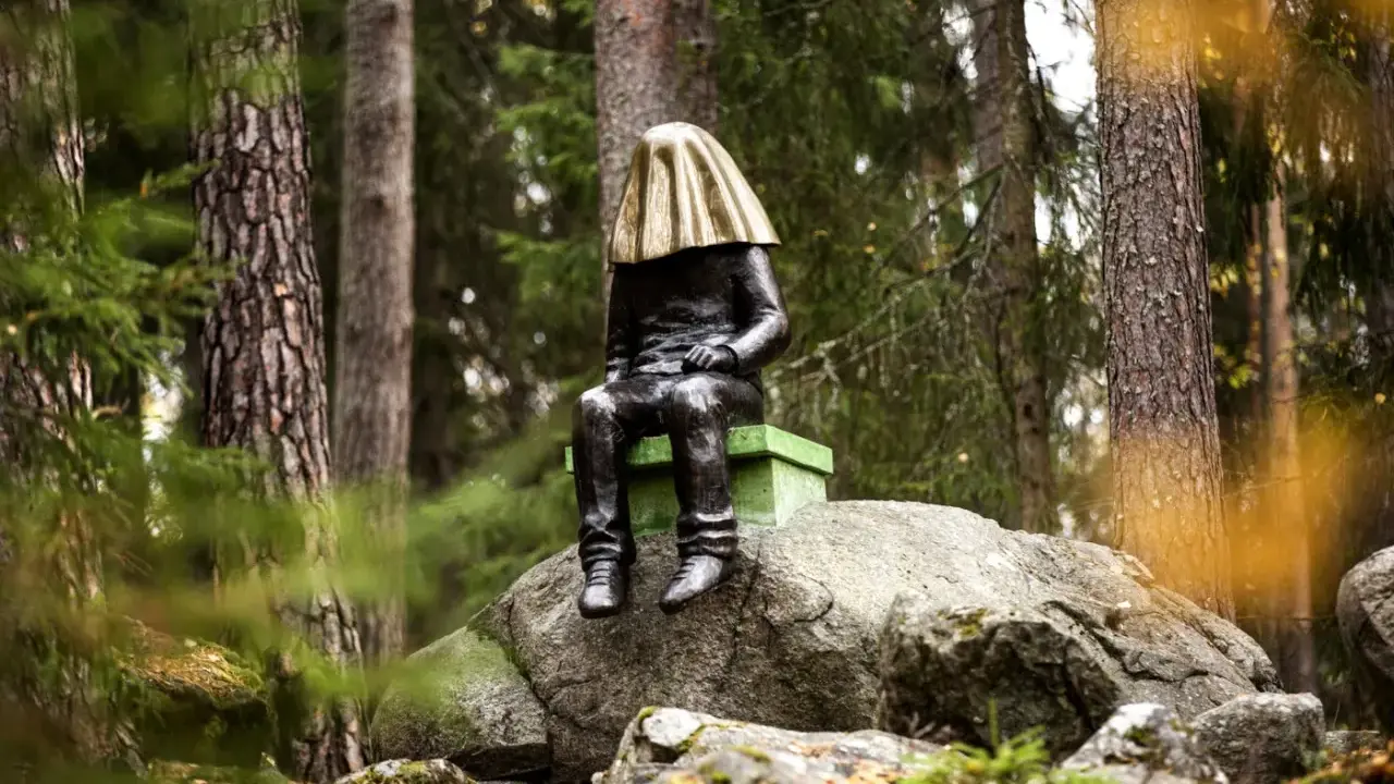 En mystisk staty med gyllene tyg över huvudet sitter på en sten i **stadsparken Falun**.