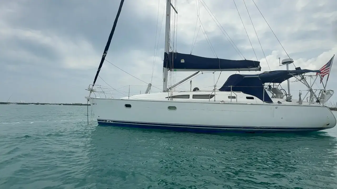 Voilier blanc à l'ancre, voiles bleues repliées. Un avis sur le Sun Odyssey 37, prêt pour l'aventure.
