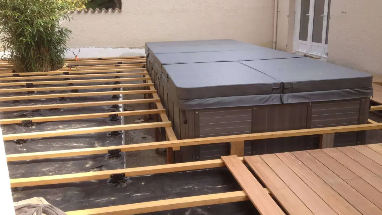 Construction d'une terrasse en bois autour d'un spa. L'espacement des plots sur le plot béton est visible, prêt pour les lames de bois.