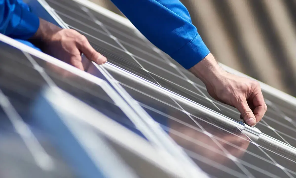 Händer i blå arbetskläder monterar solpaneler från Longi Solar på ett tak.