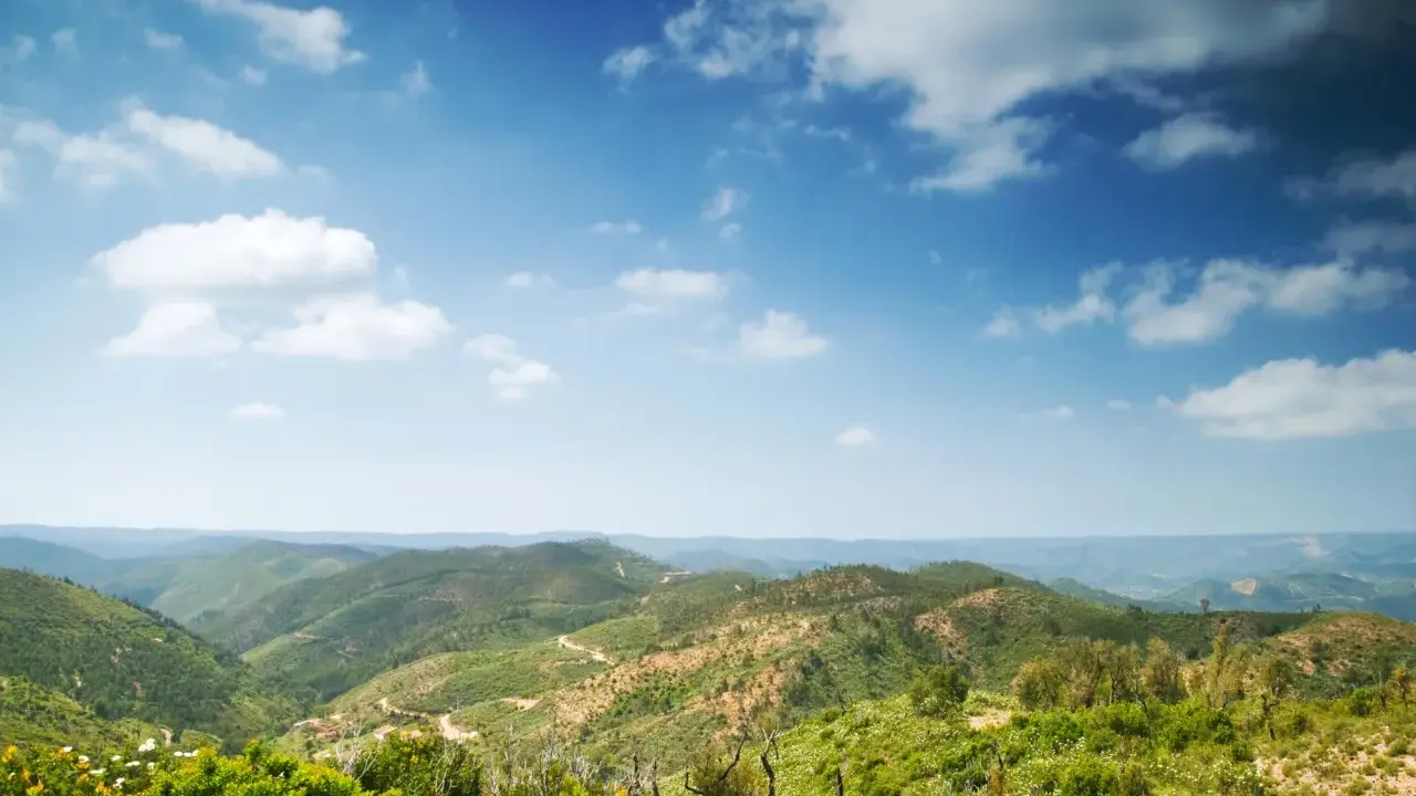 Grüne Hügel und Täler in Monchique, Portugal, unter einem weiten Himmel mit weißen Wolken.