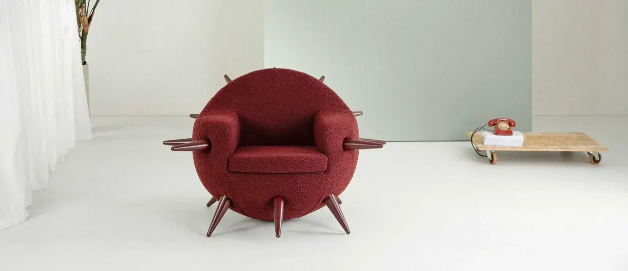 A round, burgundy armchair with pointed legs and armrests, in a minimalist room.