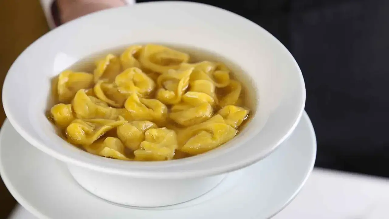 Un piatto fumante di tortellini in brodo, un classico comfort food italiano, servito in una ciotola bianca.
