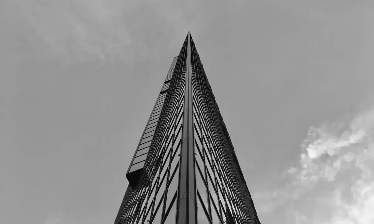 Minimalistyczne fotografowanie architektury. Ostry szczyt wieżowca przecina niebo, odbijając chmury w szklanej fasadzie.