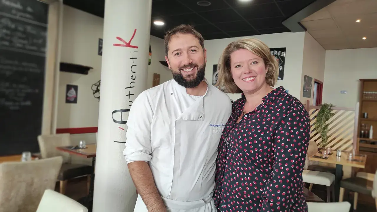 Le chef et sa collègue sourient devant la colonne "Authentik St Grégoire". L'ambiance chaleureuse du restaurant est palpable.