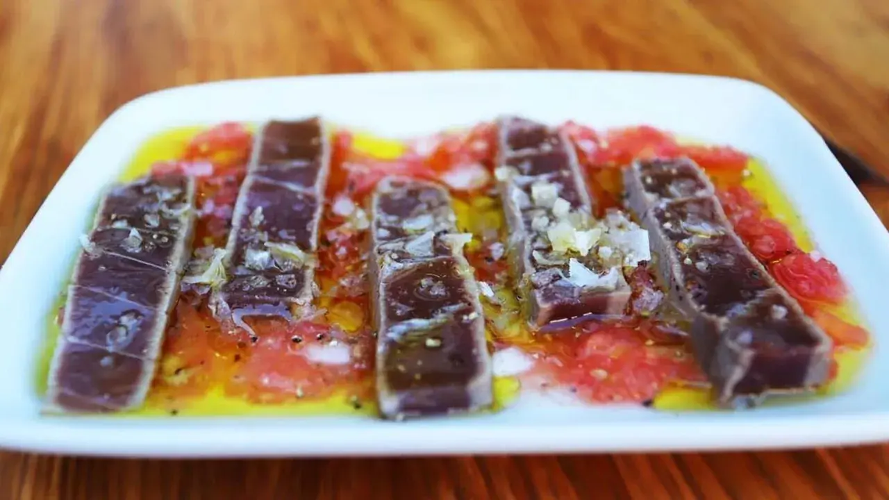 Tiras de atún marinado sobre rodajas de tomate y cítricos, un delicioso plato de comida típica de Huelva.