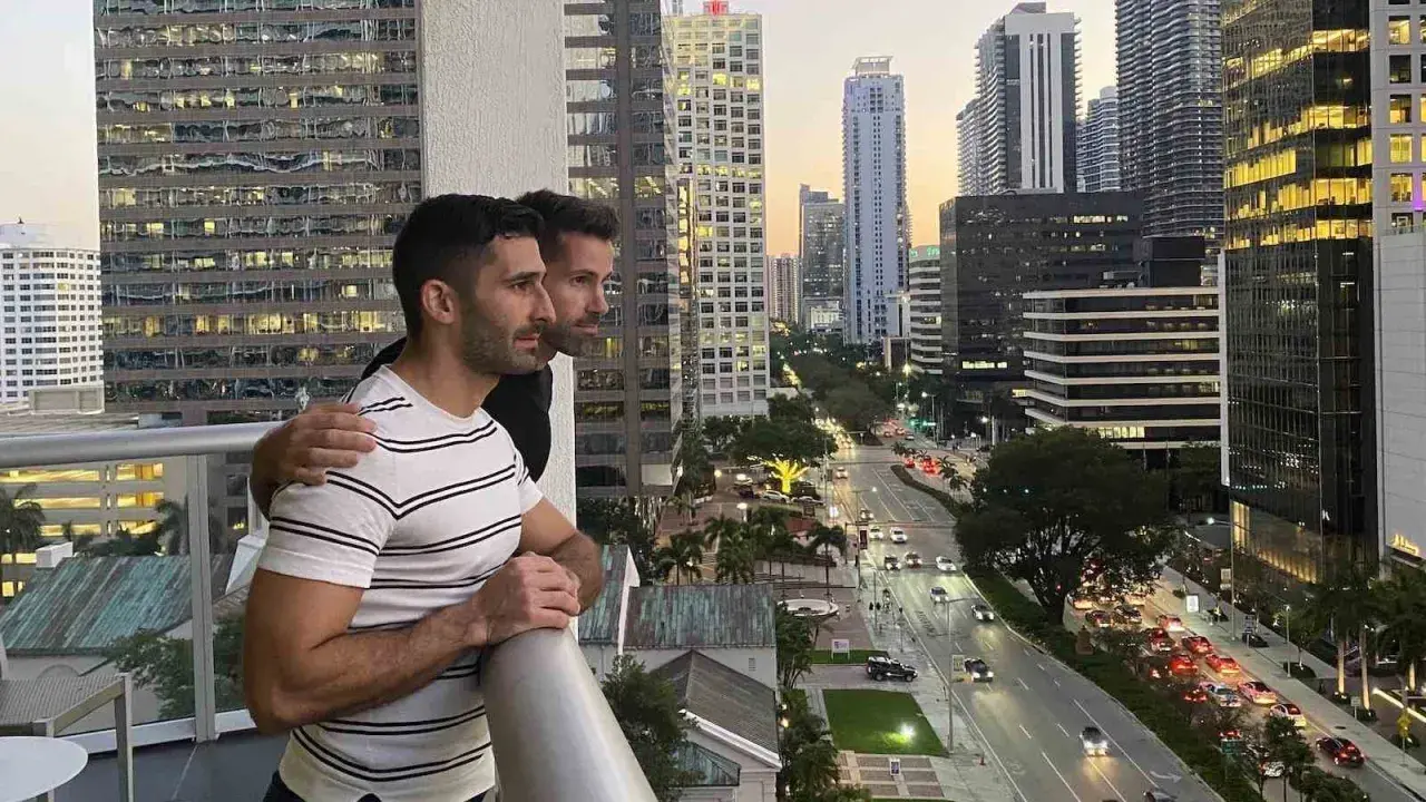 Two men embrace on a balcony overlooking a city street, a scene reminiscent of some of the most gay cities in the US.