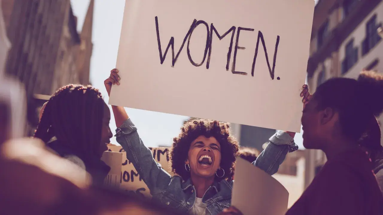 Frauen demonstrieren für Gleichberechtigung. Eine Frau hält ein Schild mit der Aufschrift "WOMEN". Das zeigt, was feminist ist: eine Stimme für Frauen.