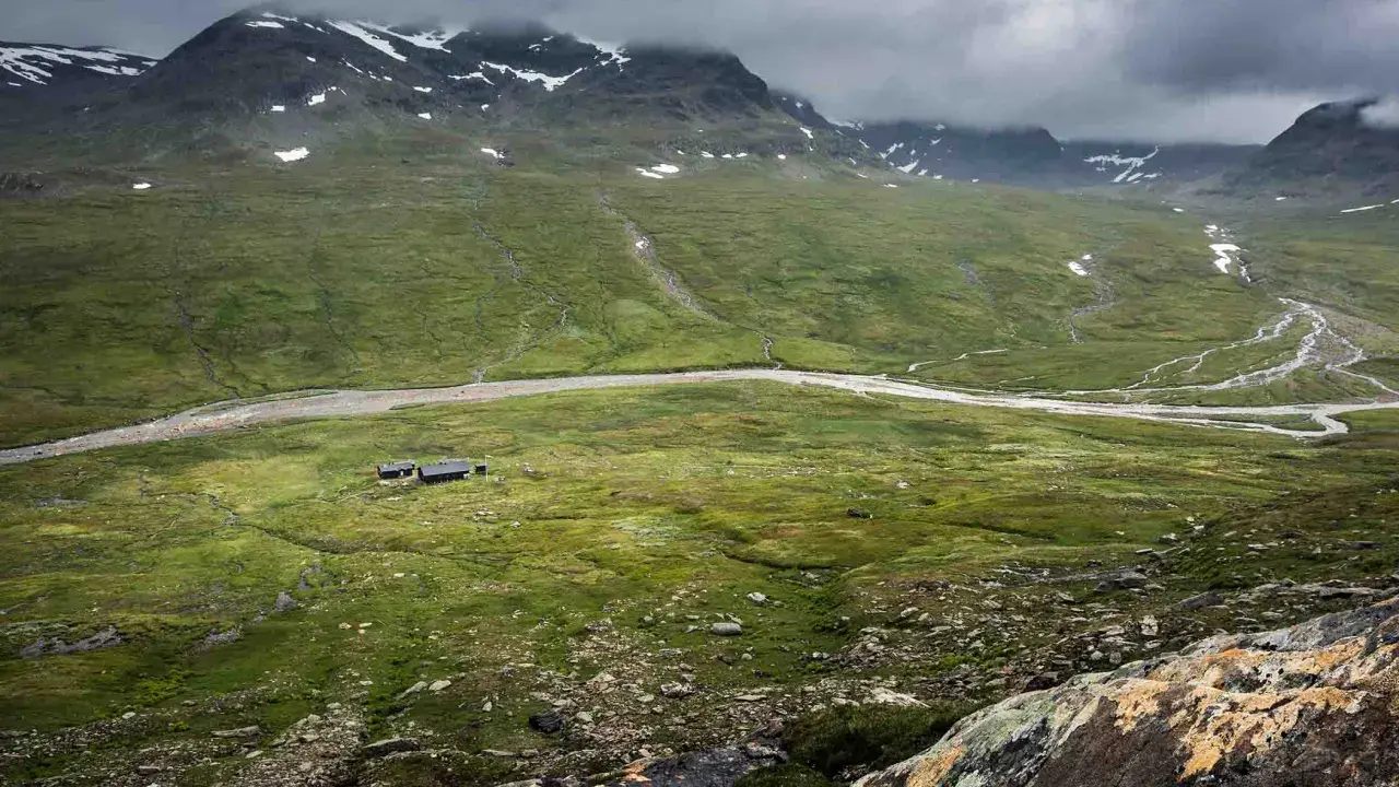 Vacker vy över fjällandskap med snöklädda toppar, en slingrande älv och stugor vid Kungsleden nära Hemavan.
