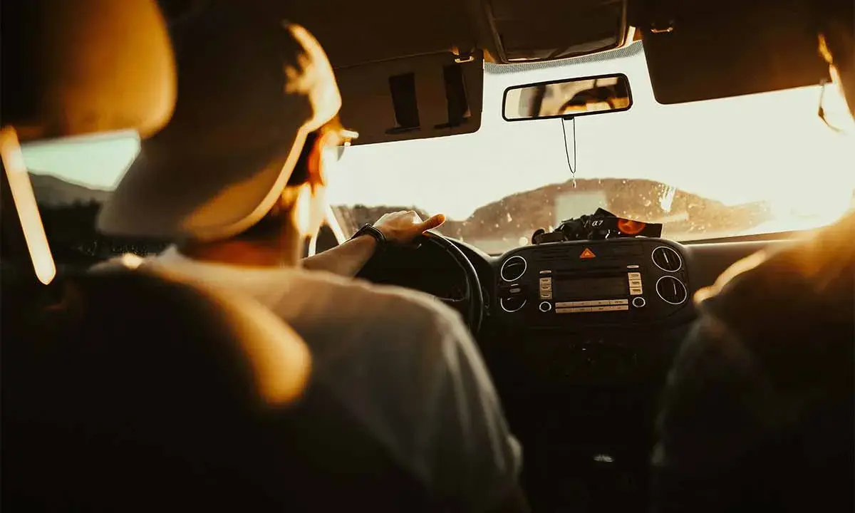 Hombre con gorra al volante, listo para planificar viaje en coche. El sol ilumina el interior del vehículo.