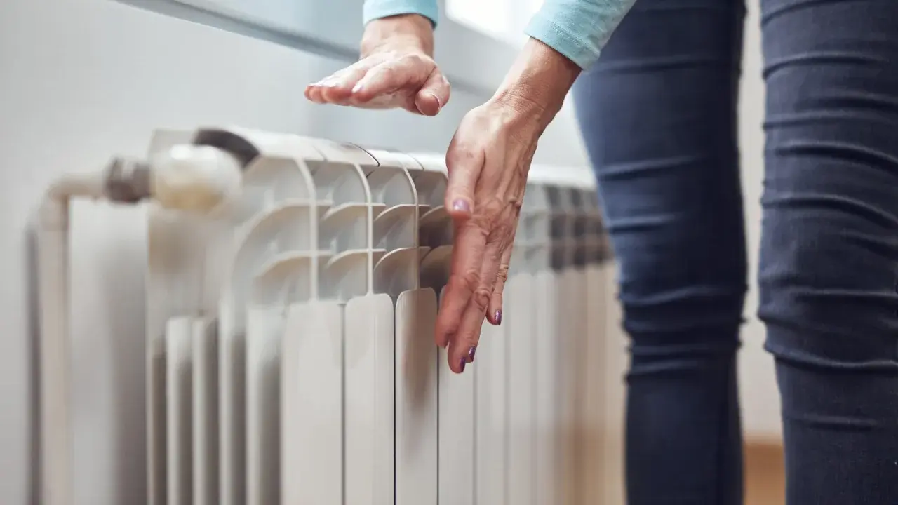 Dłonie sprawdzają temperaturę grzejnika, zastanawiając się, dlaczego grzejnik jest zimny na dole.