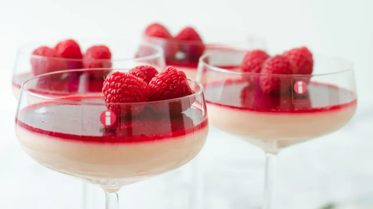 Flera glas med krämig pannacotta, toppad med hallon och en röd sås. En perfekt dessert i glas.