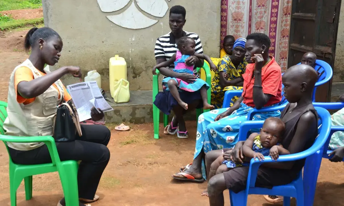 Kvinnor och barn samlas för vaccination i Uganda. En kvinna i väst visar upp papper.