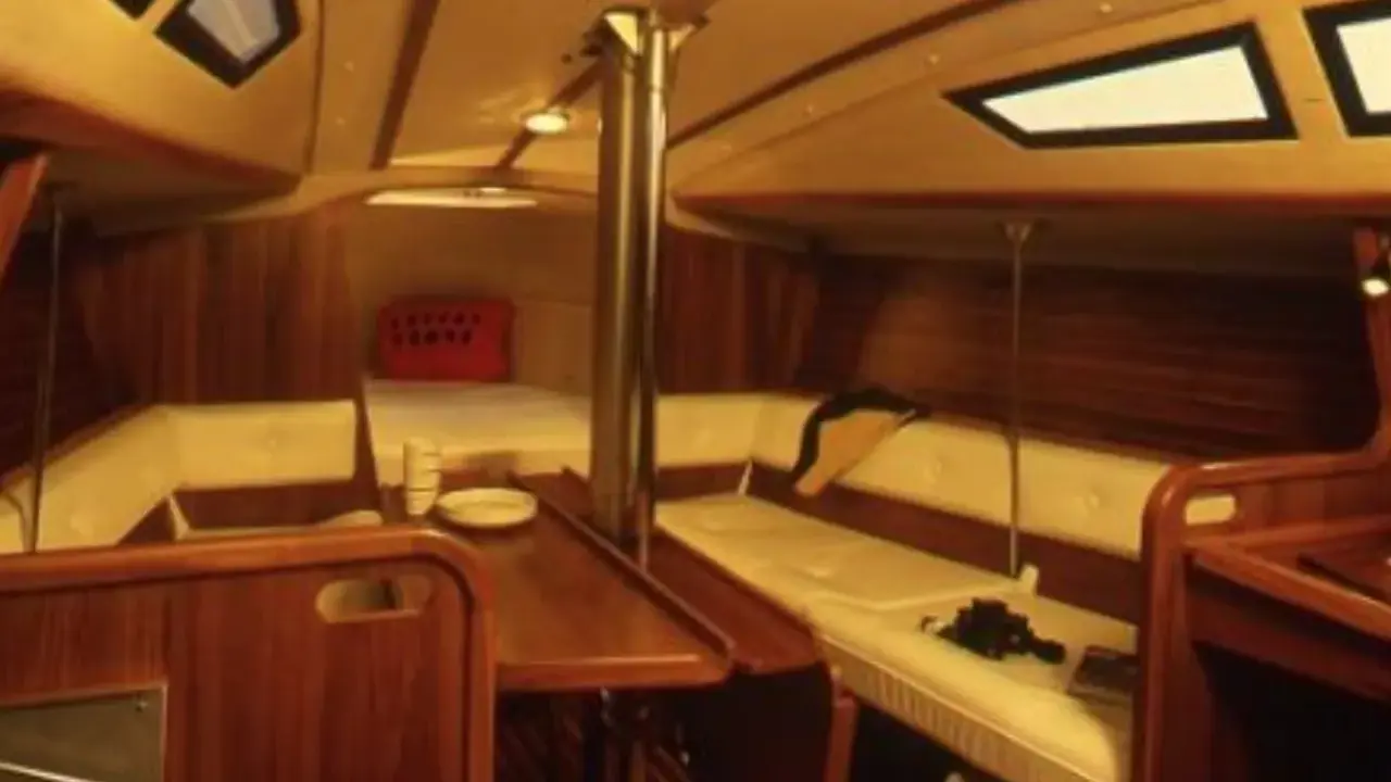 Intérieur chaleureux d'un voilier, avec banquettes en cuir crème, boiseries sombres et hublots. Le **selection 37 interieur** offre un espace confortable pour la vie à bord.