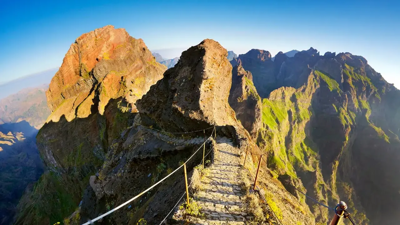 Pfad über Felsen zum Pico Ruivo, Madeira. Steile Hänge, grüne Vegetation und ein schmaler Weg mit Seilsicherung.