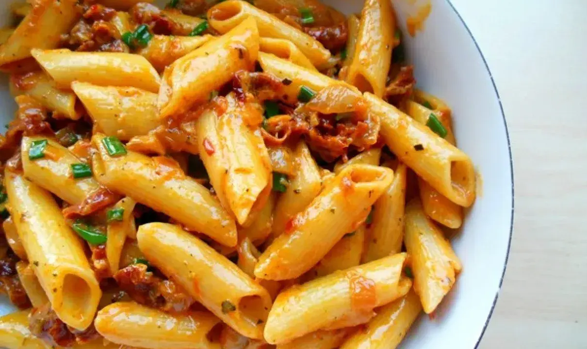Penne z sosem z suszonych pomidorów i zieloną cebulką, danie wygląda apetycznie.