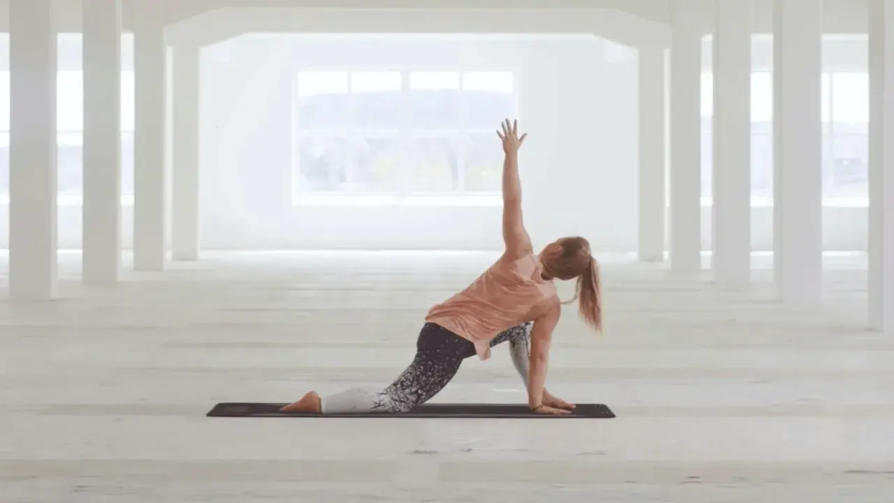 Kvinna utför en vriden yogaställning i ett ljust, öppet rum. Hon fokuserar på sin power yoga-träning.