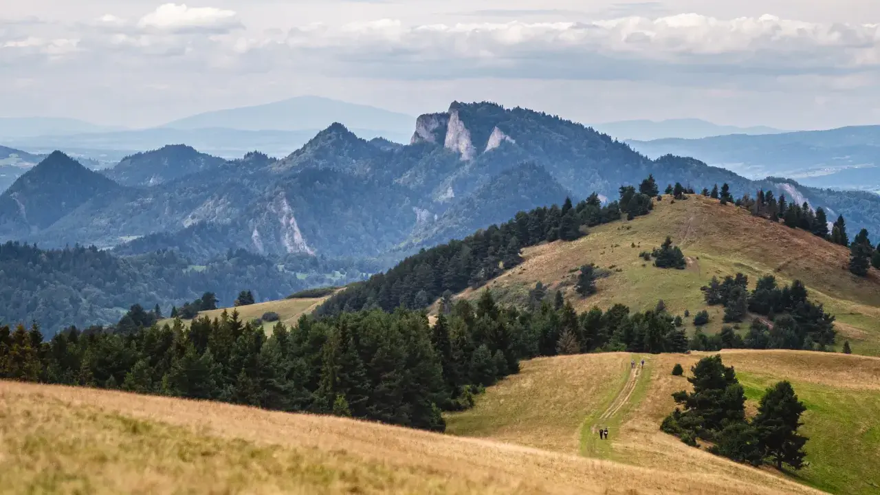 Malowniczy krajobraz górski, idealny na szczawnica trasę. W oddali skaliste szczyty, bliżej zielone wzgórza i ścieżka dla turystów.