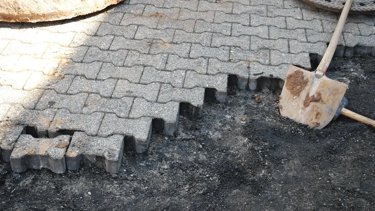 Fragment nawierzchni z kostki brukowej w trakcie układania, obok łopata.