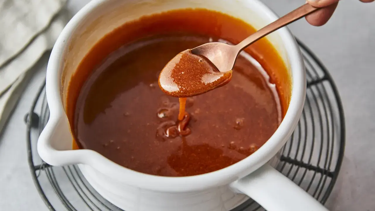 Flüssiges Karamell tropft von einem Löffel in einen Topf. Das Zucker karamellisieren ist fast perfekt.