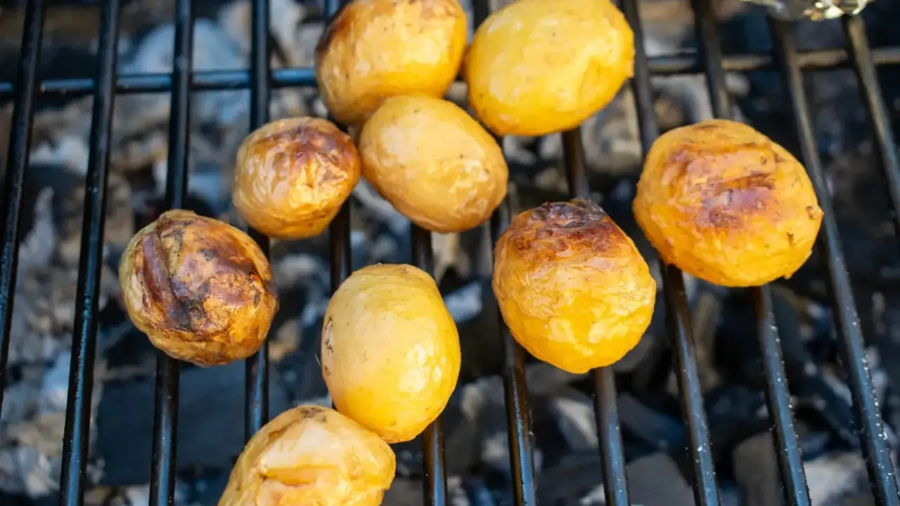 Kleine, goldbraune Kartoffeln garen auf dem Grillrost über glühender Kohle. Sie sind bereit für ein leckeres Abendessen.