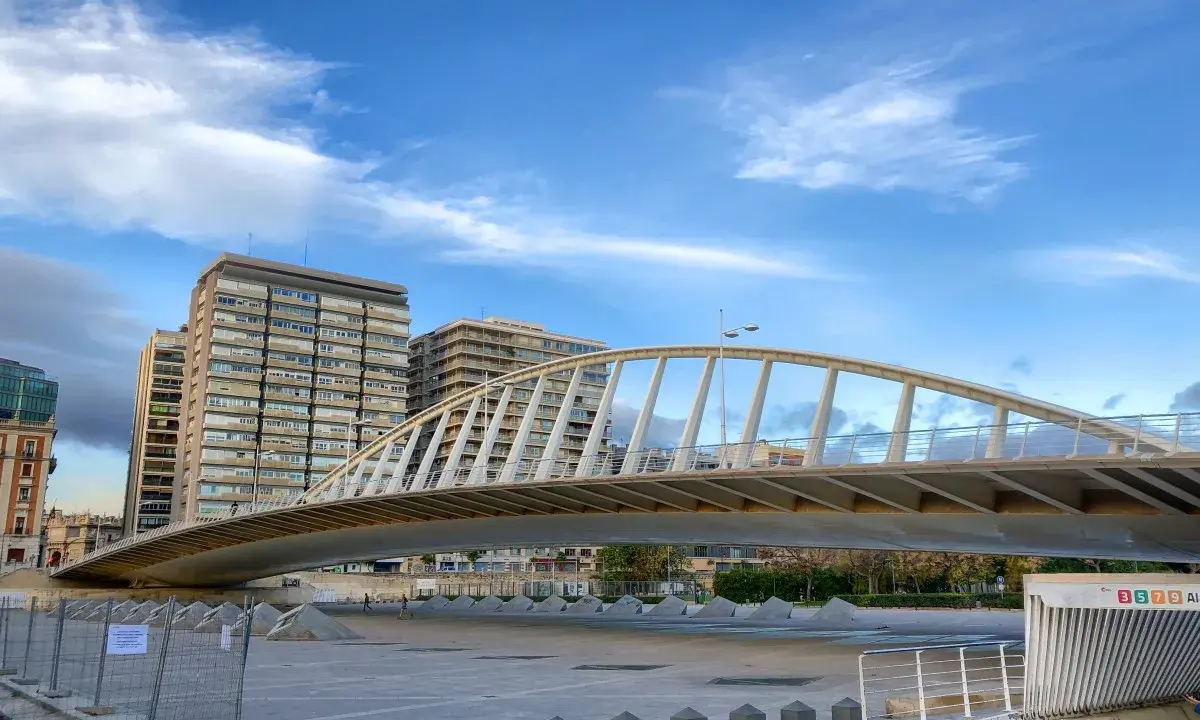 El moderno puente de la Exposición cruza un río, con edificios altos al fondo bajo un cielo azul con nubes.