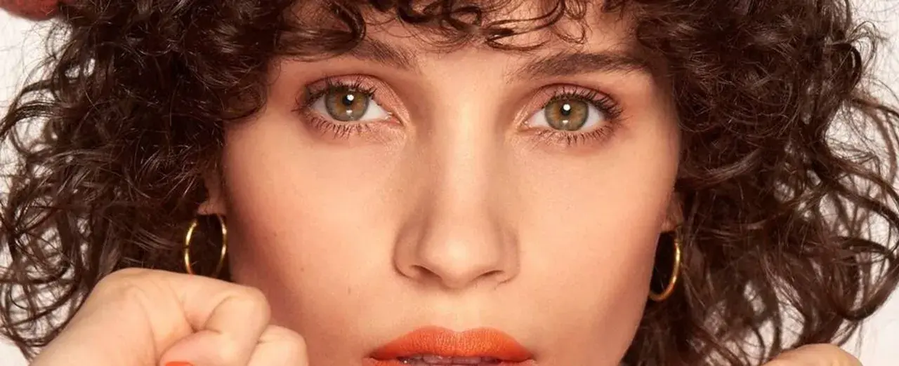 Primer plano de una mujer con rizos oscuros y maquillaje color coral vibrante en los labios.