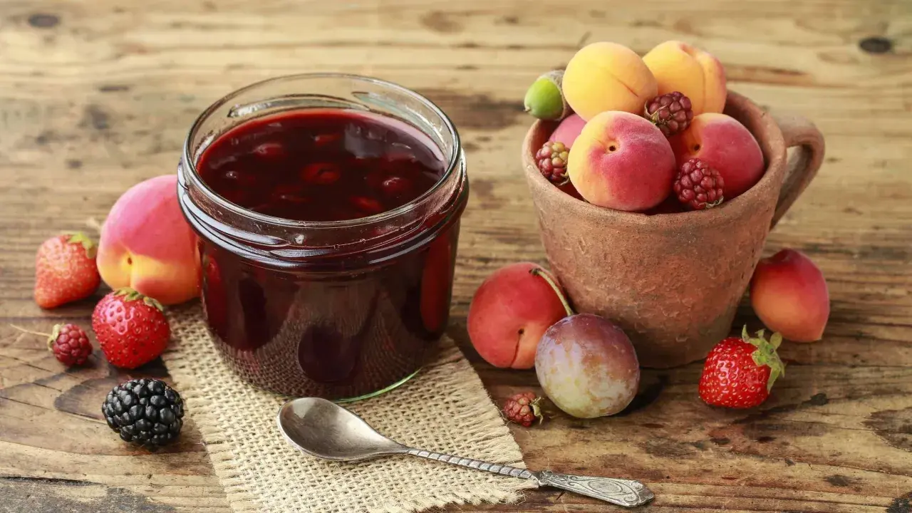 Ein Glas selbstgemachte Marmelade mit frischen Früchten daneben. Die Frage "wie lange ist selbstgemachte Marmelade haltbar" beschäftigt viele Hobbyköche.