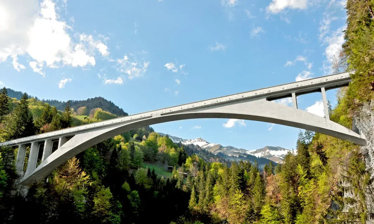 El puente de Salginatobel se alza majestuoso sobre un valle verde, con picos nevados al fondo.