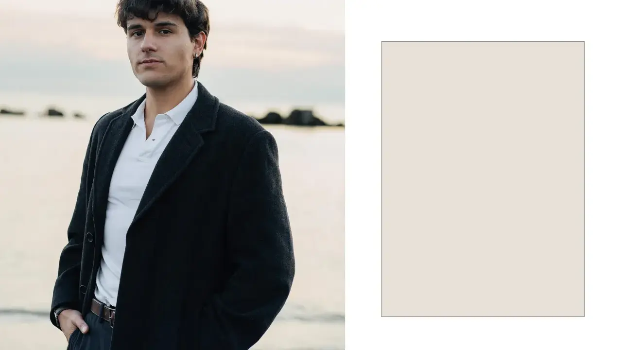 Davide Avolio, con le mani in tasca, indossa un cappotto scuro e una polo bianca, con il mare sullo sfondo.