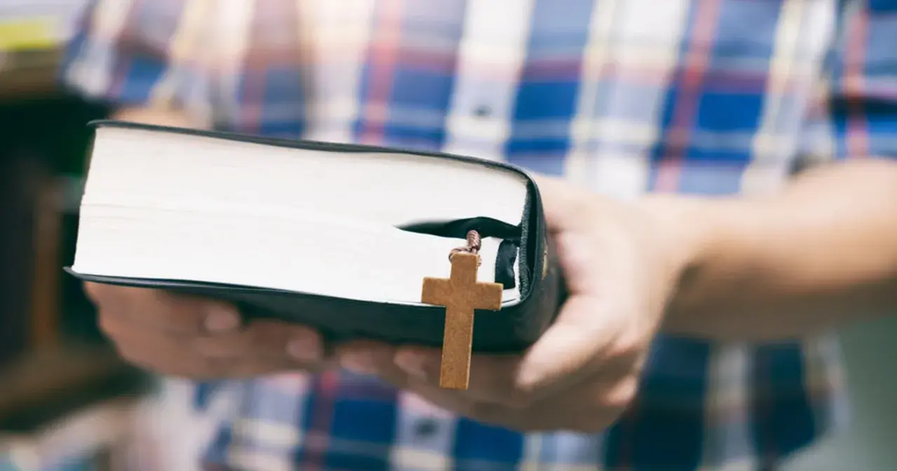 Osoba w kratę trzyma Biblię z drewnianym krzyżem, symbolizującym dwa przykazania miłości.
