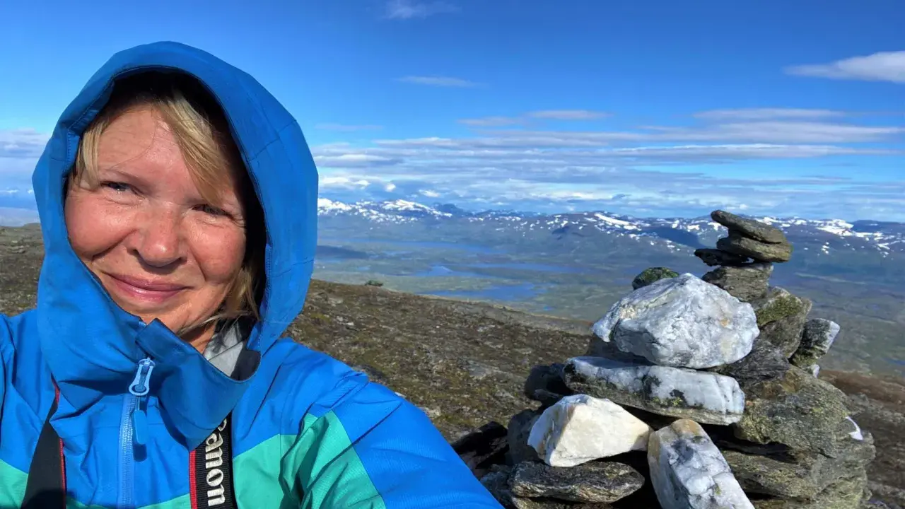 Kvinna på berg i Sverige med en stenröse i förgrunden och snöklädda berg i bakgrunden.
