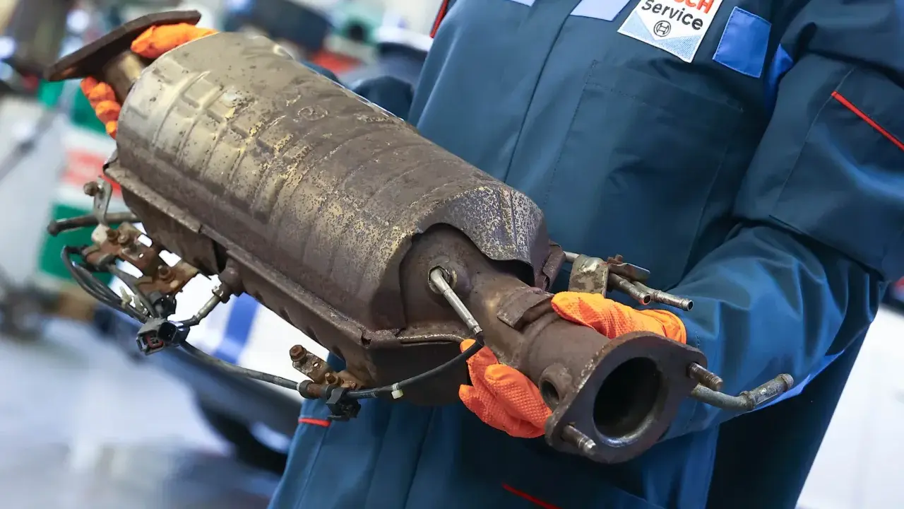Mechanik w rękawiczkach trzyma zużyty katalizator, prawdopodobnie z Peugeota p2448.