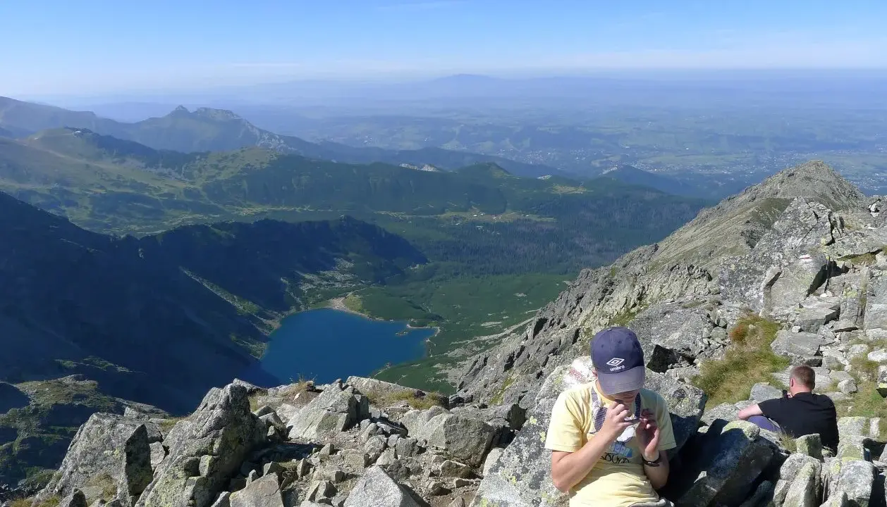 Widok na Tatry z żlebu Kulczyńskiego. W dole jezioro, na pierwszym planie odpoczywający turyści.