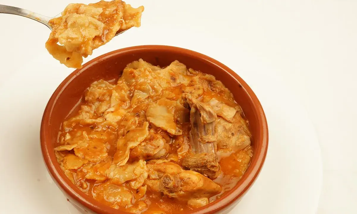 Un plato humeante de comida típica de Albacete, con trozos de carne y pasta en una salsa rojiza.