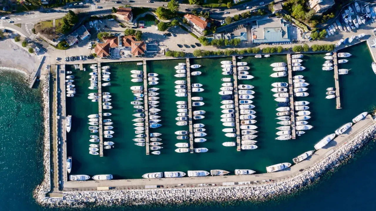 Widok z lotu ptaka na port w Chorwacji, pełen białych jachtów i łodzi zacumowanych w turkusowej wodzie.
