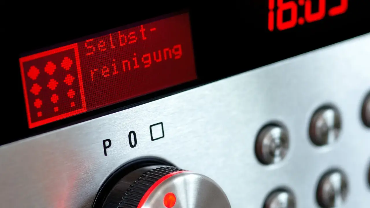 Bedienfeld eines Ofens mit rotem Display, das "Selbst-reinigung" anzeigt. Daneben die Uhrzeit 16:05.