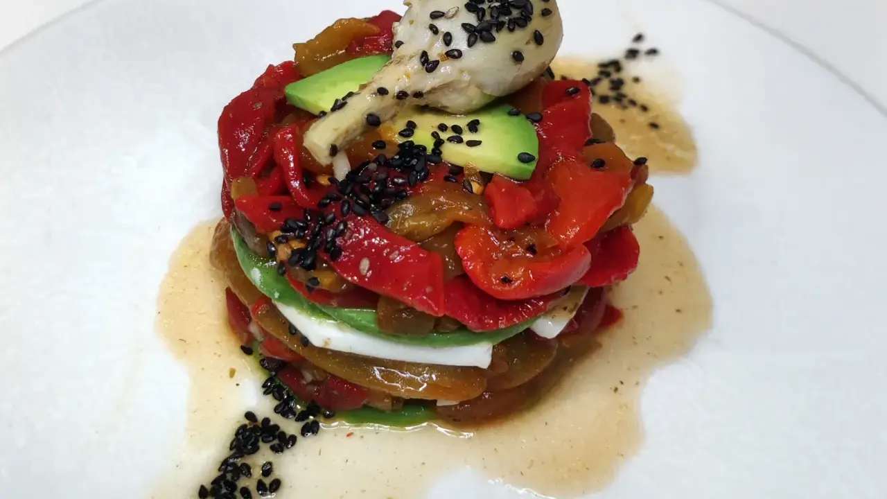 Torre de pimientos del piquillo asados, aguacate y queso fresco, coronada con un alcachofa y semillas de sésamo negro.