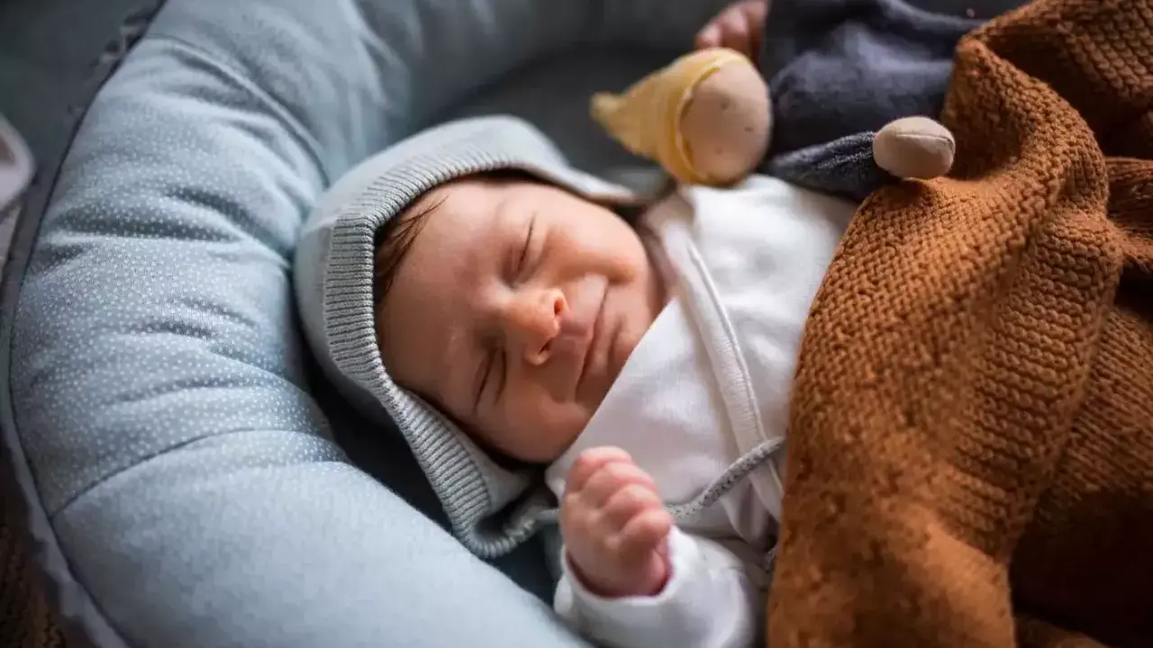 Ein Neugeborenes schläft friedlich in einer Babywippe, eingewickelt in eine warme Decke. Vielleicht ist es der 37 wochen schub, der ihm süße Träume schenkt.