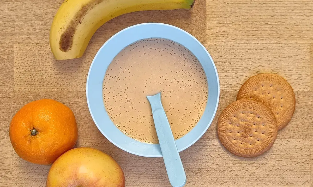Un tazón de papilla galletas maría con frutas: plátano, naranja y manzana.