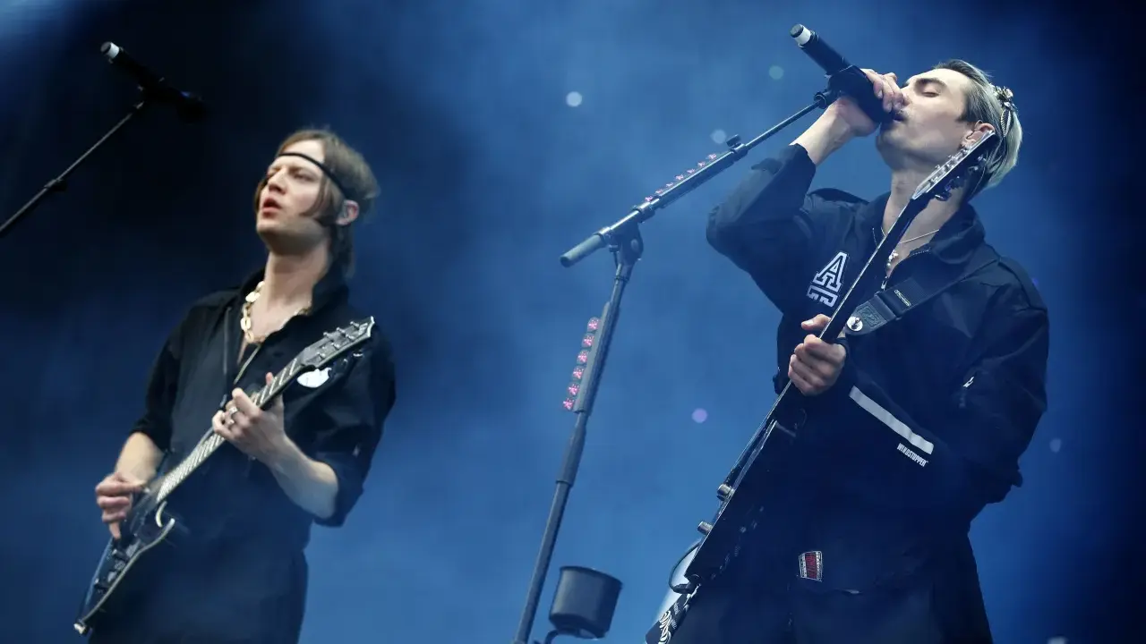 Gustaf Norén sjunger och spelar gitarr med Mando Diao på scenen, omgiven av rök och blått ljus.