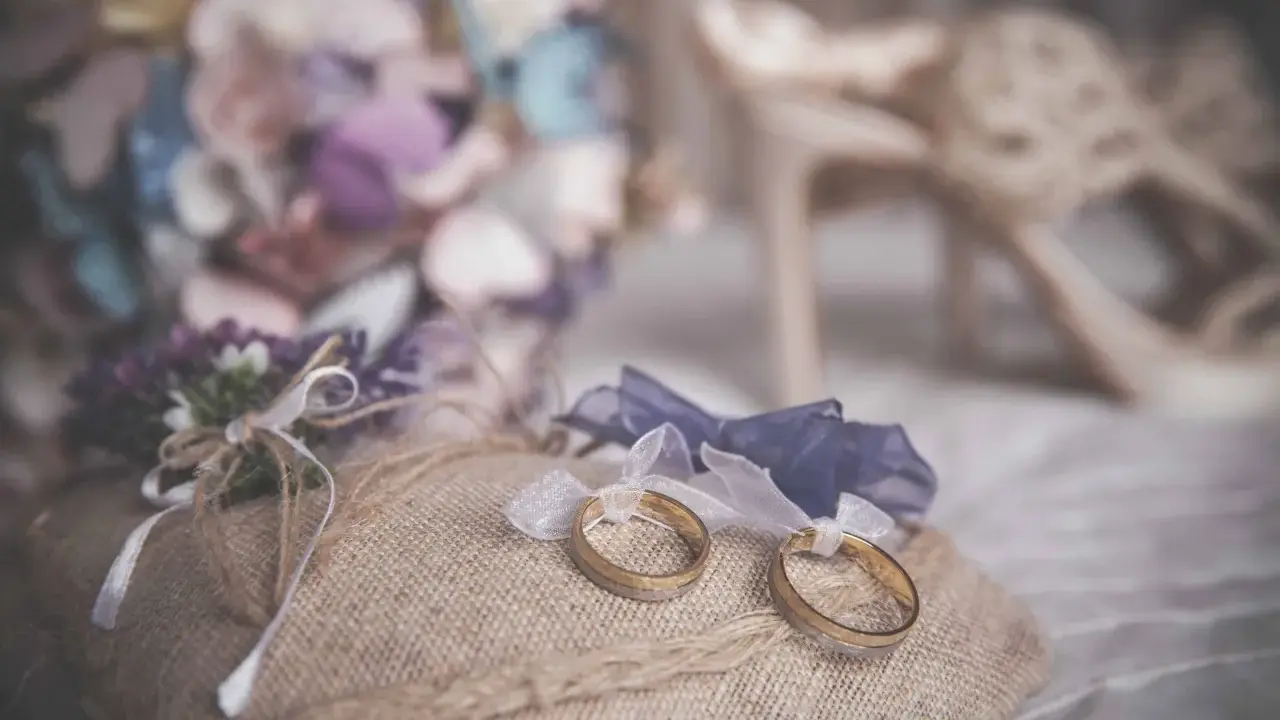 Anillos de boda sobre cojín rústico, ideas para decorar la habitación donde se viste la novia con flores y zapatos elegantes.