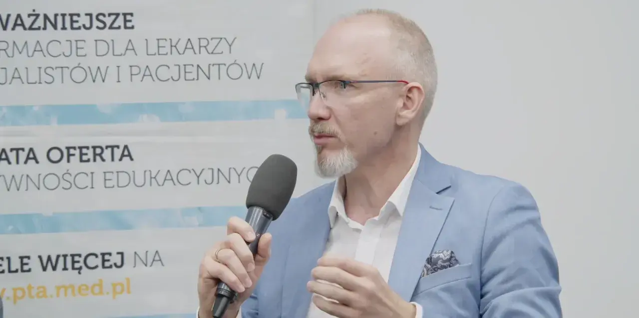 Mężczyzna w okularach i niebieskiej marynarce mówi do mikrofonu, omawiając nowe podejście do leczenia astmy, jakby to był jego własny asthma rap.