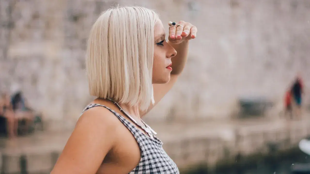 Frau mit blondem **long bob naturwelle** blickt in die Ferne, die Hand schützend über die Augen gelegt.