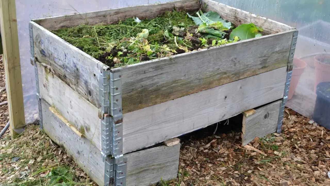 En kompost pallkrage fylld med grönt avfall och jord. Den gamla träkonstruktionen är robust och redo att omvandla trädgårdsrester till näringsrik kompost.